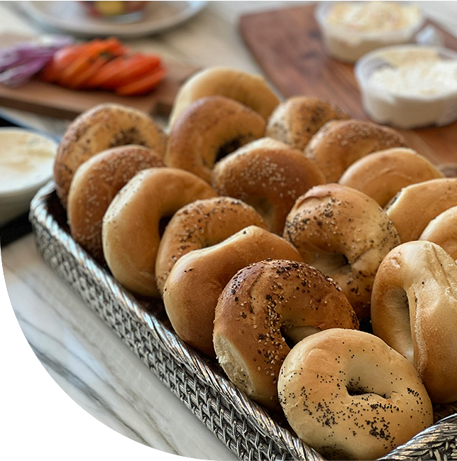 A tray of assorted bagels with cream cheese in the background.