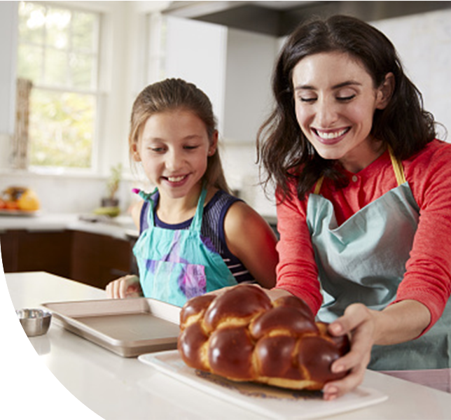A woman and a girl joyfully bake bread together in a sunlit kitchen.